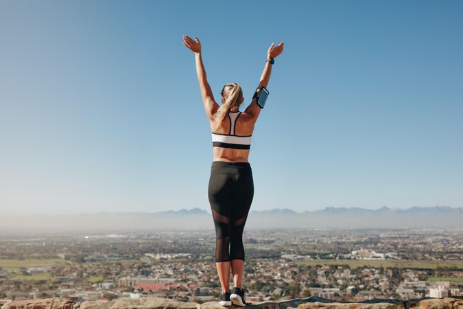 Woman in fitness wear standing on the edge of a hill looking at the city below