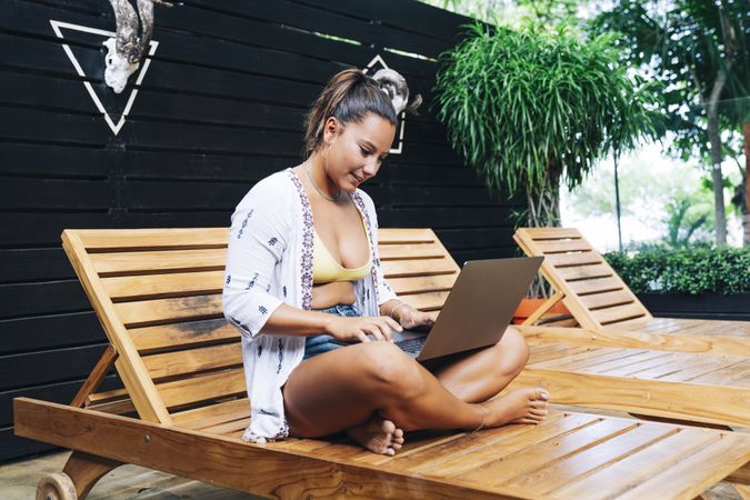 Relaxed woman using laptop while resting on deck chair