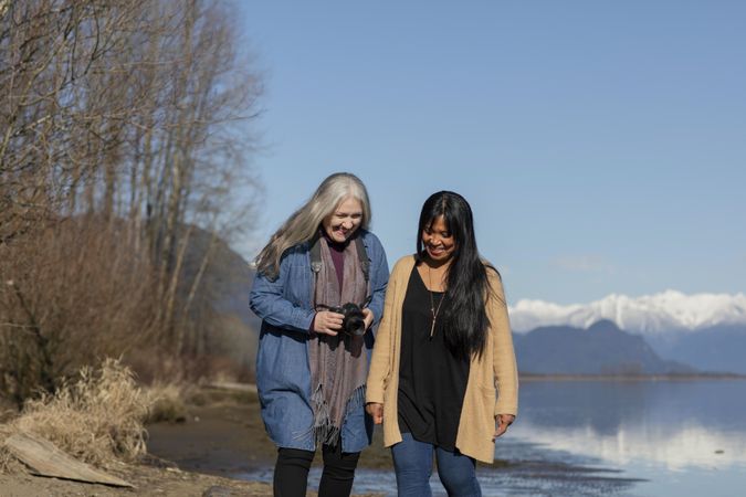 Happy woman holding camera and walking with friend outdoors
