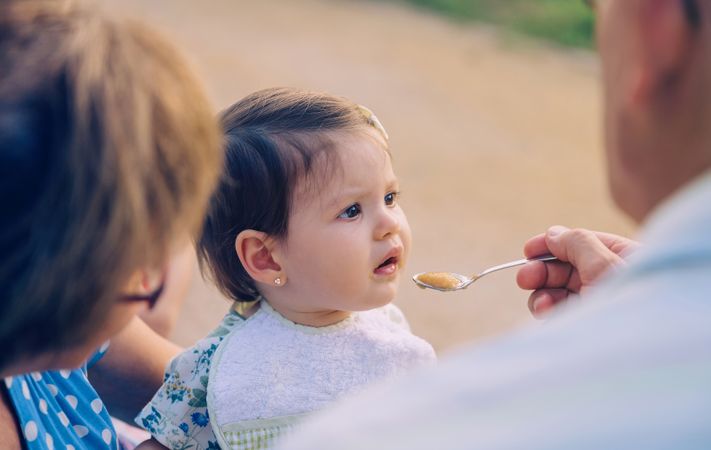 Cute baby girl being fed by grandparents outside