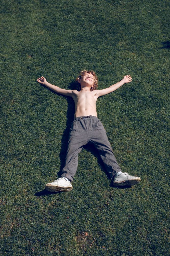 Content boy with hands and legs apart on lawn