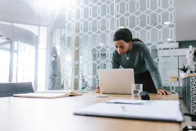 Woman executive standing by conference table and looking at her laptop