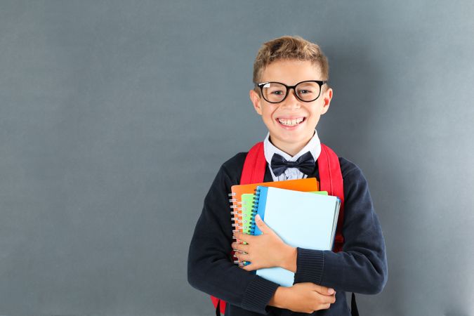 Boy in school uniform with copybooks against board, space for text