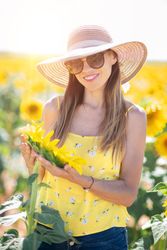 Woman in straw hat gazing while standing on bright sunflower field