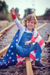 Cheerful boy with American flag sitting on railroad