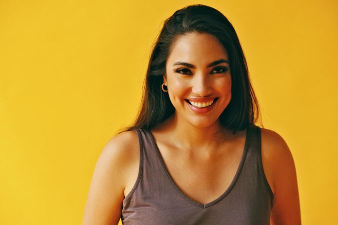 Headshot of happy Hispanic woman looking at camera with yellow background, copy space