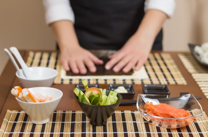 Hands of female chef ready to prepare sushi rolls, with fresh ingredients in the foreground