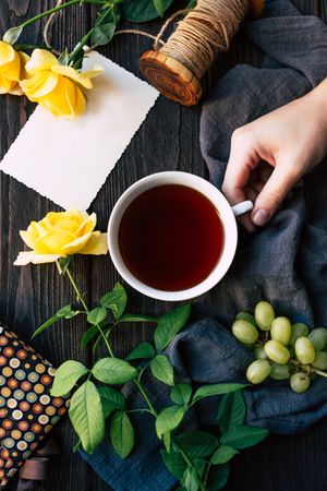 Crop hand with tea near flowers and blank note