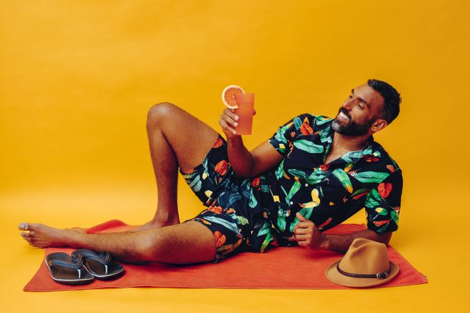 Black male laying back on towel and smiling while holding tropical drink