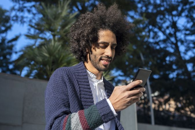 Smiling Black man using his smartphone while outside in the sun