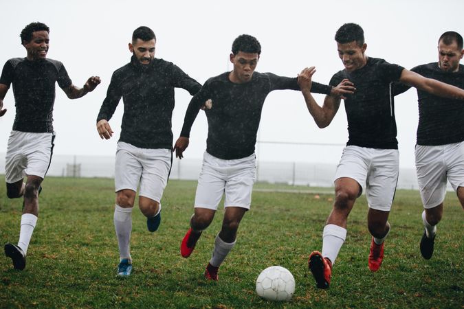 Men playing soccer running after a football on a rainy morning