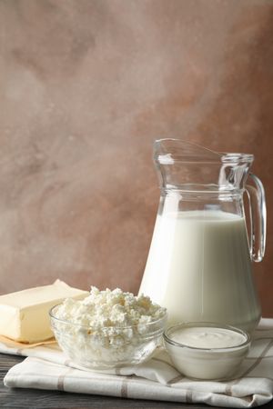 Milk, cottage cheese and butter on wooden table against brown background