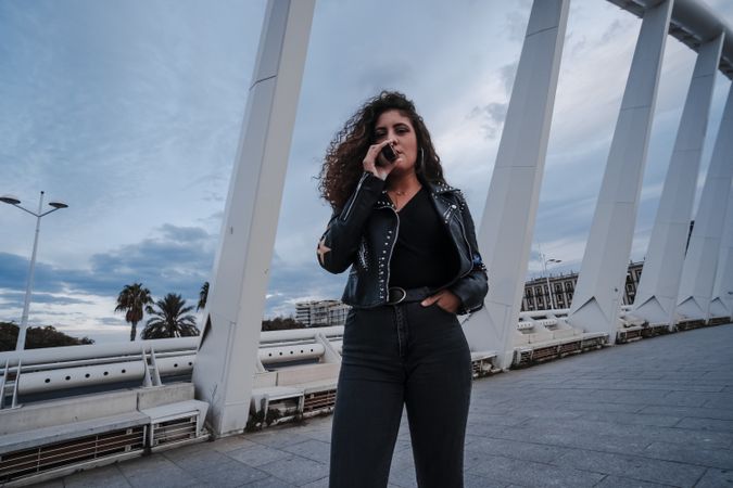 Stylish woman in jacket and jeans smoking on bridge
