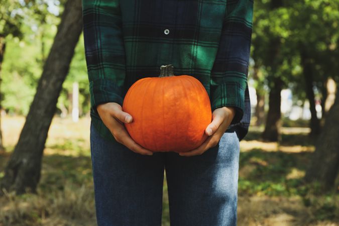Woman in shirt and jeans hold pumpkin outdoor