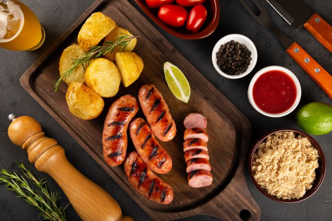 Top view of grilled sausages on wooden board served with potatoes, lime and rosemary garnish