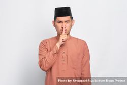 Muslim man in kufi cap making “shhh” gesture with hand over mouth 5nell0