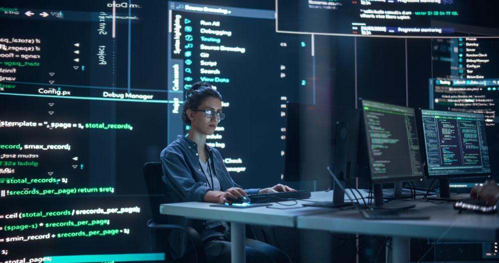 Portrait of Woman Working on Computer, Typing Lines of Code that Appear on Big Screens Surrounding her in Dark Monitoring Room.