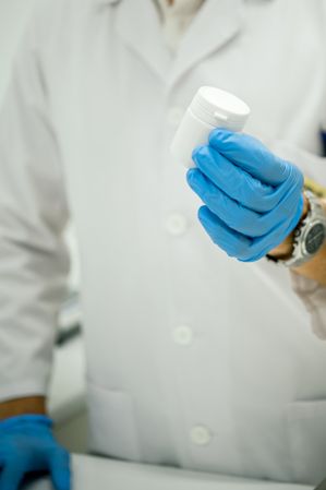 Crop pharmacist holding jar with pills in lab