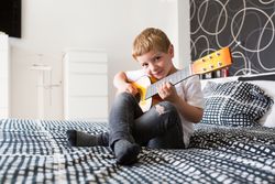 Young blonde boy playing toy guitar