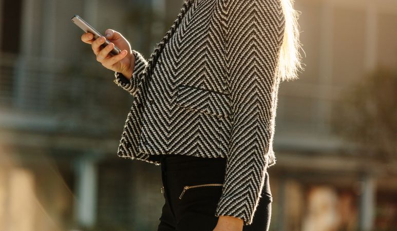 Businesswoman checking mobile phone while walking on street to office