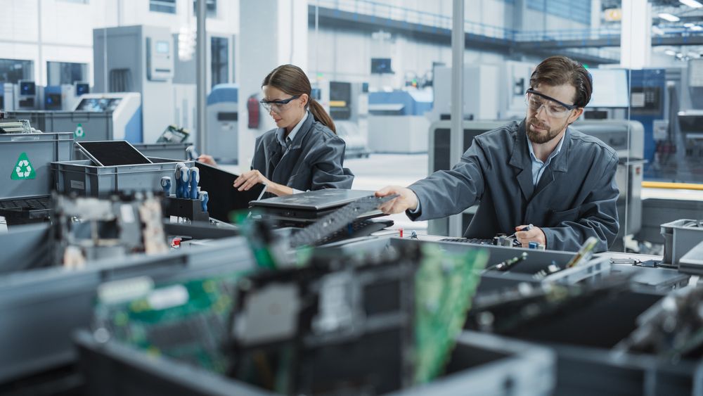 Male And Female Employees Taking Apart Old Laptops To Recycle Components For Sustainable Production Of Electronic Devices At Electronics Factory.