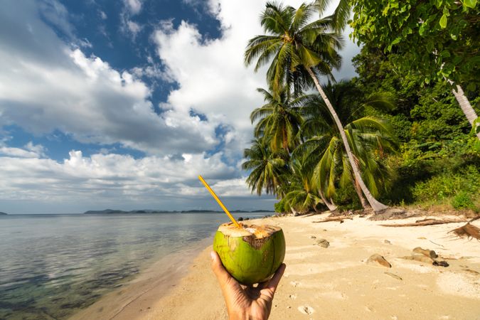 Hand with coconut drink on sandy beach