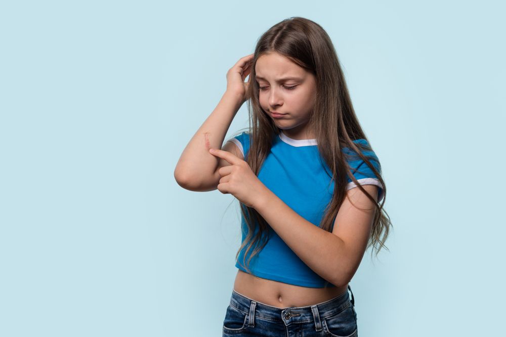 Young girl examining cut on elbow, looking concerned