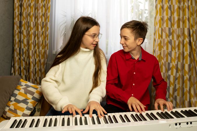 Girl and boy playing piano together while sharing joyful moment.