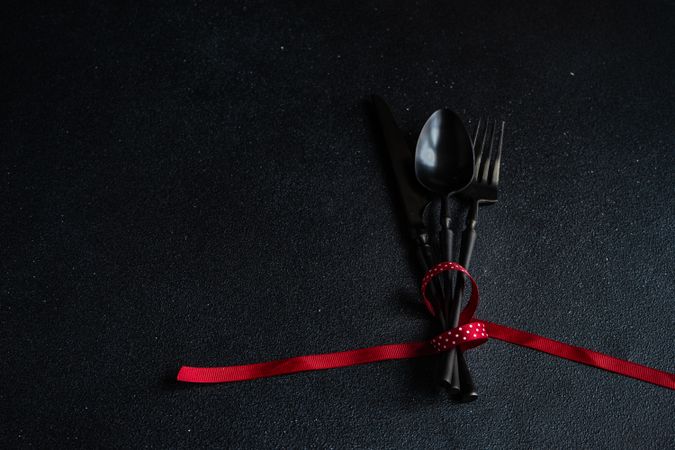 Dark cutlery on dark background tied with festive red ribbon