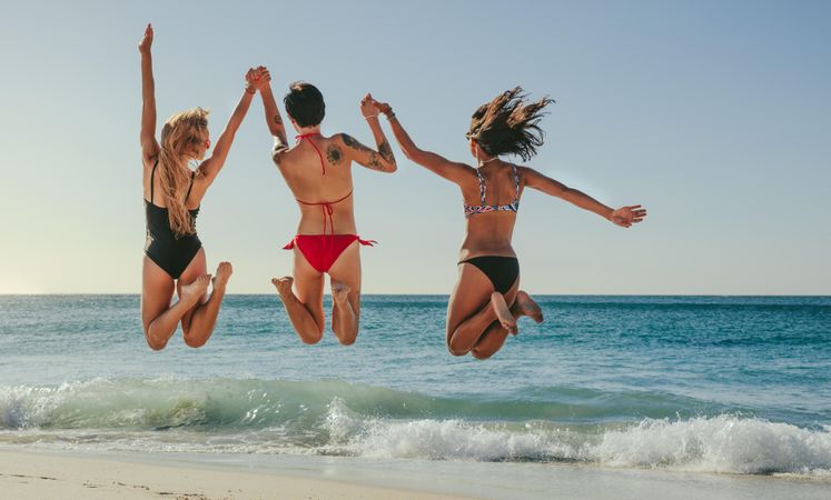 Women on summer vacation enjoying at beach jumping in air facing the sea