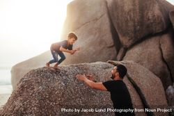 Happy little boy jumping into his father's arms from a rock 5w1rAb