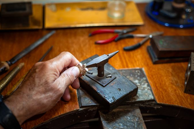 Goldsmith creating and repairing in his crafting gold jewelry workshop with an anvil. Jeweler working in a silver jewel.