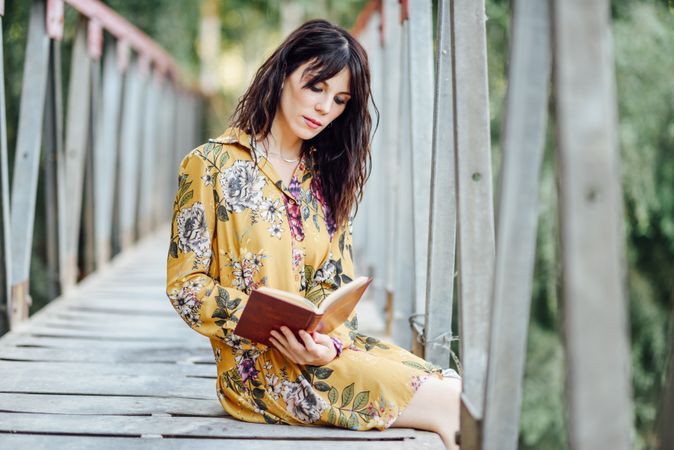 Female sitting on a rural bridge and reading