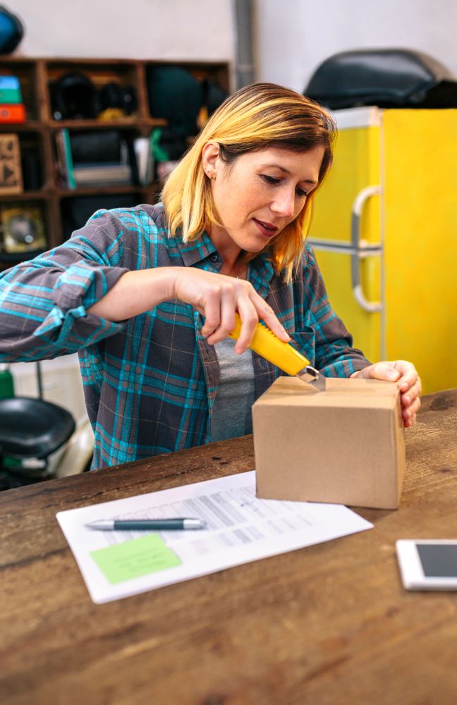 Blonde woman with cutter unpacking order received by courier with merchandise to sell on line