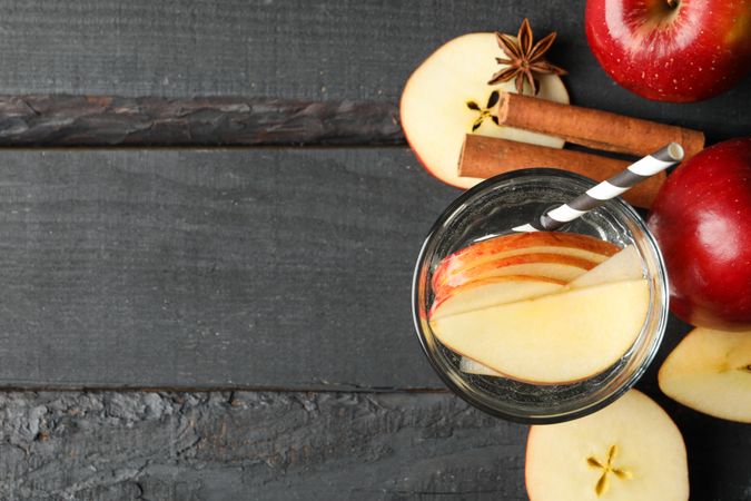 Top view of glass of water with straw, apple slices and cinnamon slices with copy space