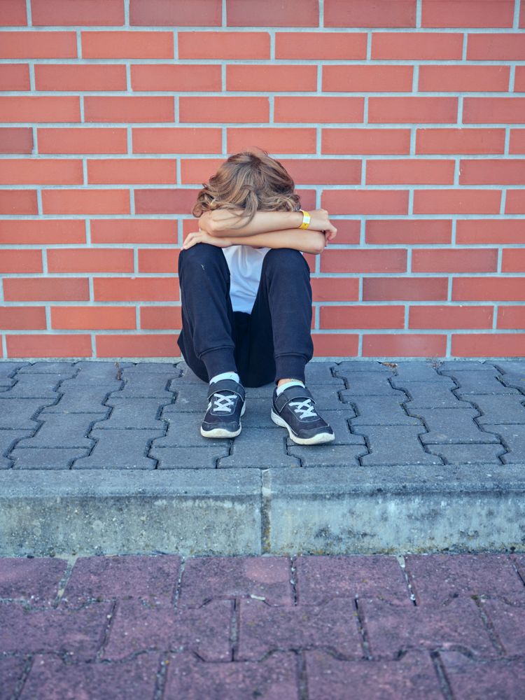 Unrecognizable boy hugging knees and sitting near brick wall