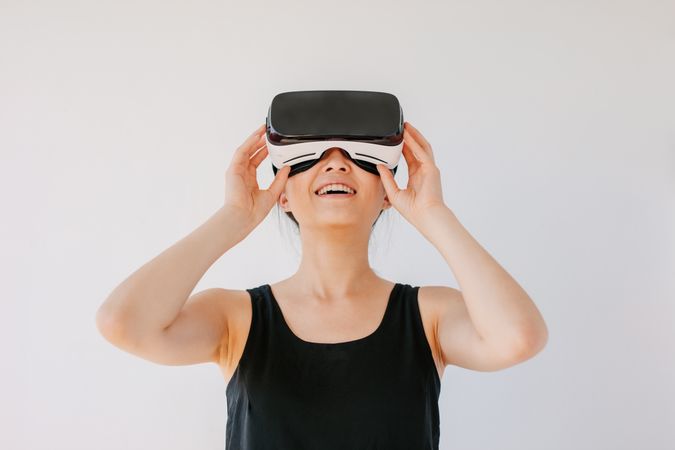 Young woman using the virtual reality headset and smiling against grey background