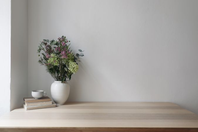Vase with floral bouquet with eucalyptus tree branches, hydrangea, wax flowers next to cup of tea