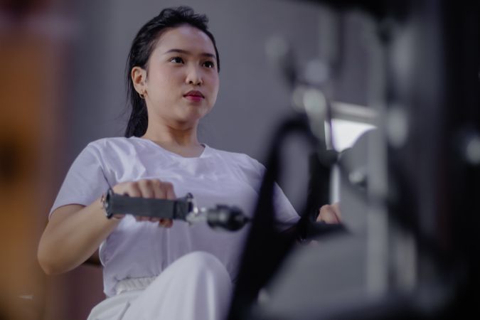 Dedicated asian woman exercising on rowing machine at the fitnes