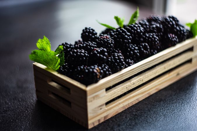 Fresh raw blackberries in wooden box on stone background with mint garnish