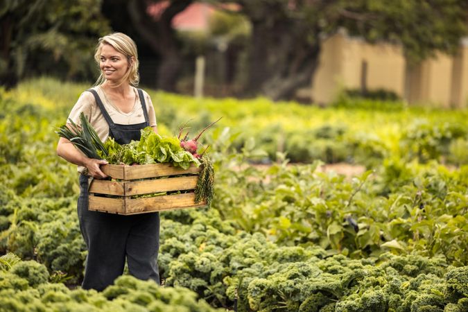 Happy farmer smiling cheerfully while walking through her vegetable garden during harvest season