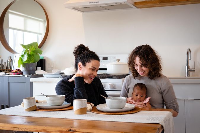 Two mothers eating soup with newborn baby at their dining table at home