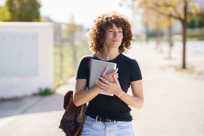 A Young Woman with Beautiful Curly Hair Walking Outdoors, Carrying a Laptop and Notebooks