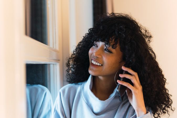 Cheerful Black woman talking smartphone at home