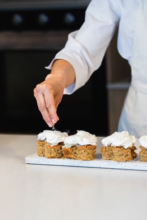 Crop baker decorating carrot cakes with cream
