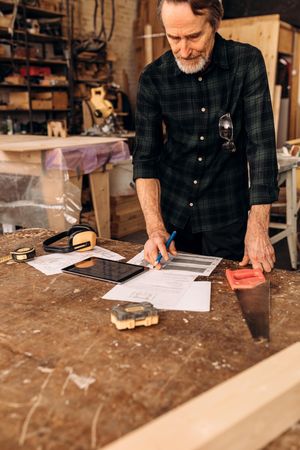 Older man with design plans in his woodwork shop, vertical