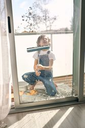Preteen boy cleaning windows with mop at home