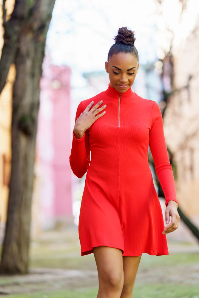 Happy female in casual red dress walking outside