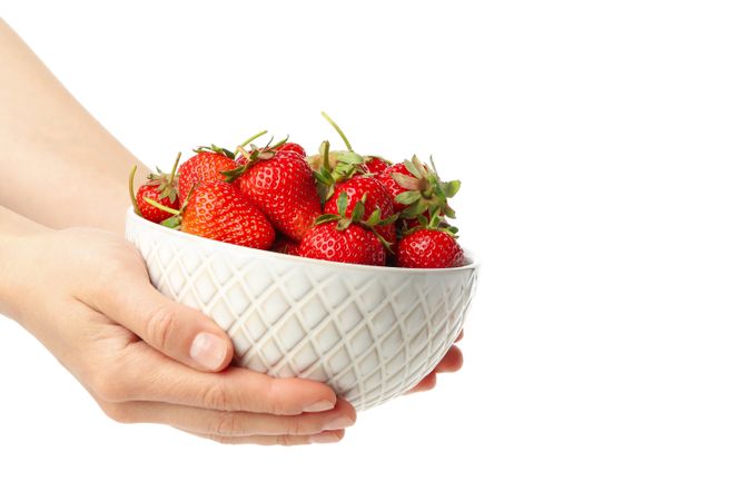 Female hands hold bowl with tasty strawberry, isolated on plain background. Summer berry