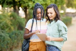Women friends pointing at something on tablet in casual clothing in park